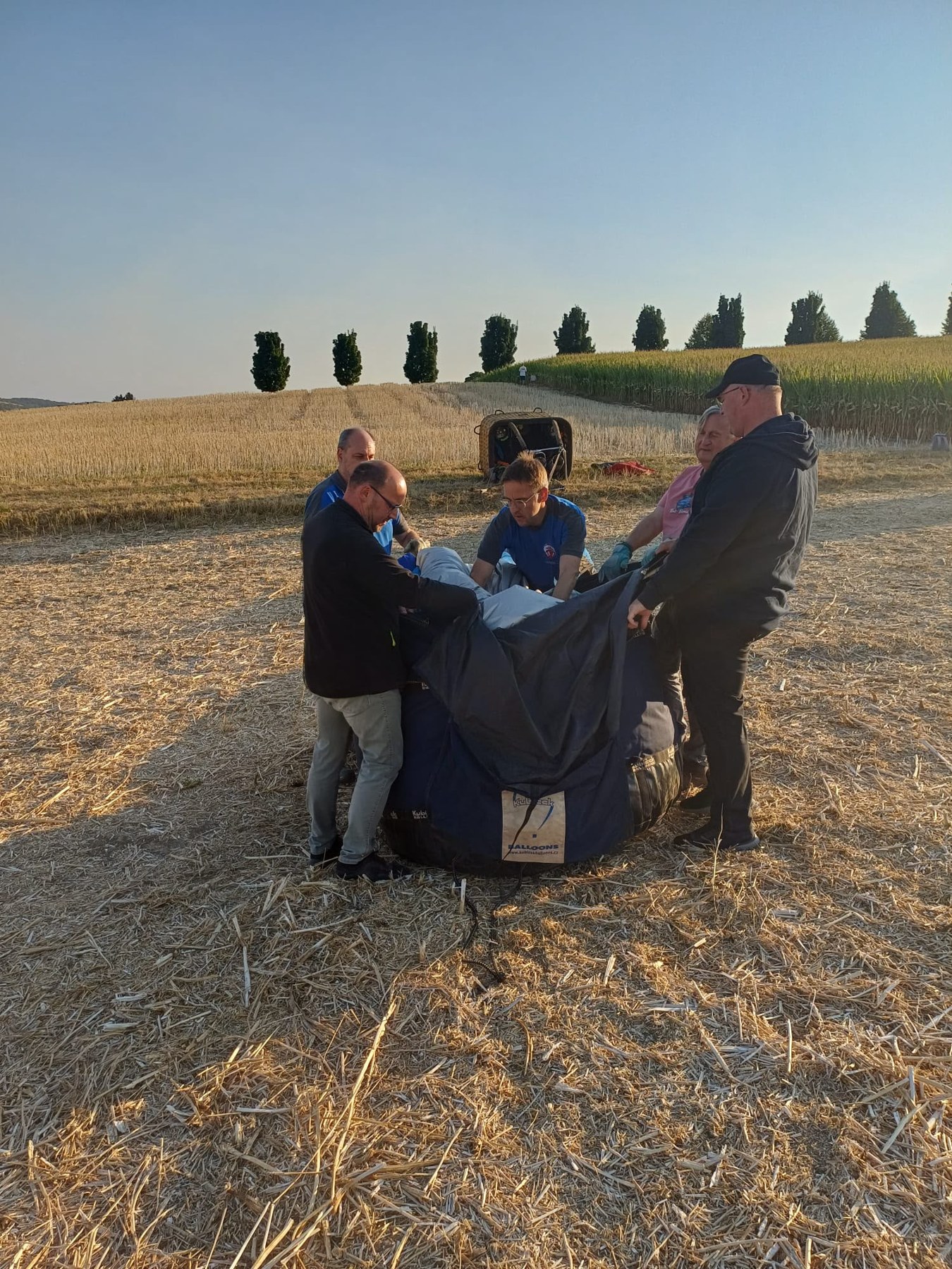 Drei Menschen packen gemeinsam die Ballonhülle auf einem Feld ein
